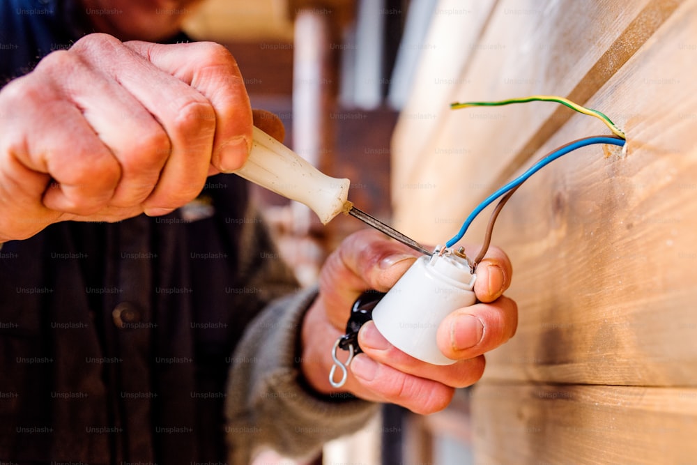 Hands of unrecognizable electrician working with screwdriver, wooden wall