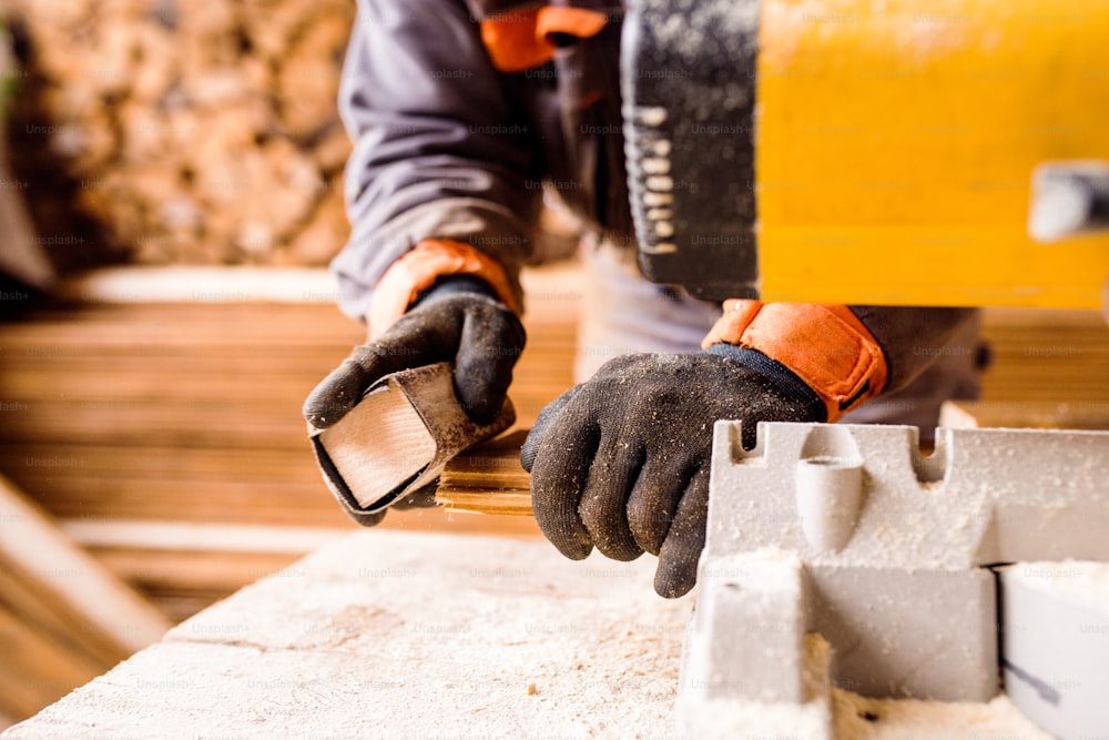 Hands of unrecognizable man grinding planks of wood for home construction.