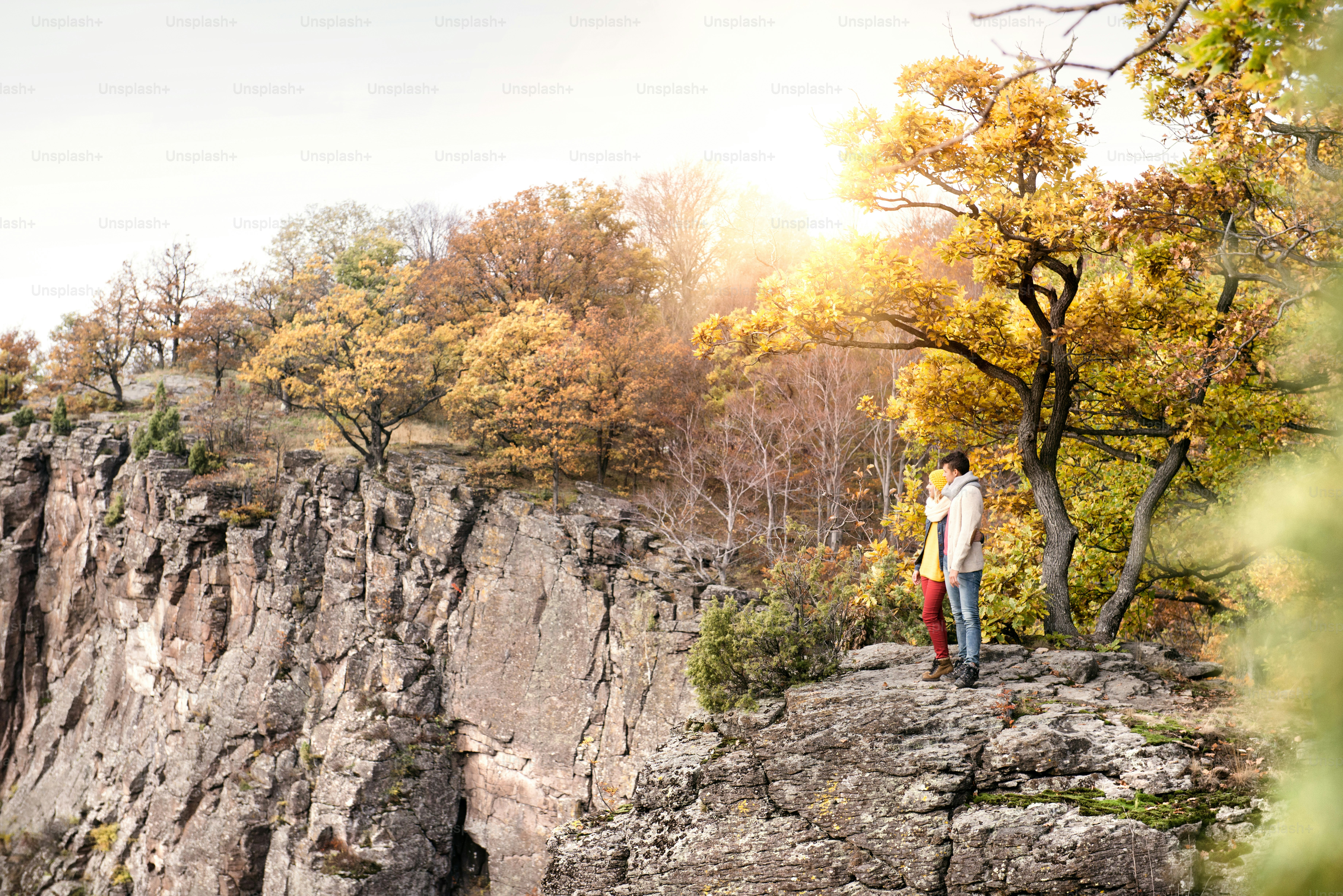 Beautiful couple in autumn nature standing on a rock against colorful autumn forest
