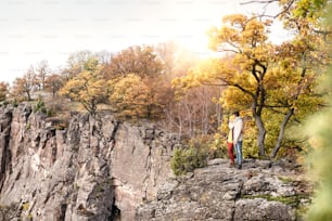 Beautiful couple in autumn nature standing on a rock against colorful autumn forest