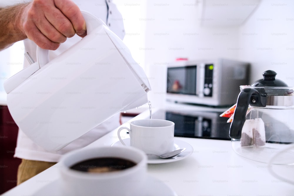 Nicht erkennbarer Mann bei der Zubereitung von Kaffee. Gießen Sie heißes Wasser aus dem Wasserkocher in vorbereitete Tassen.