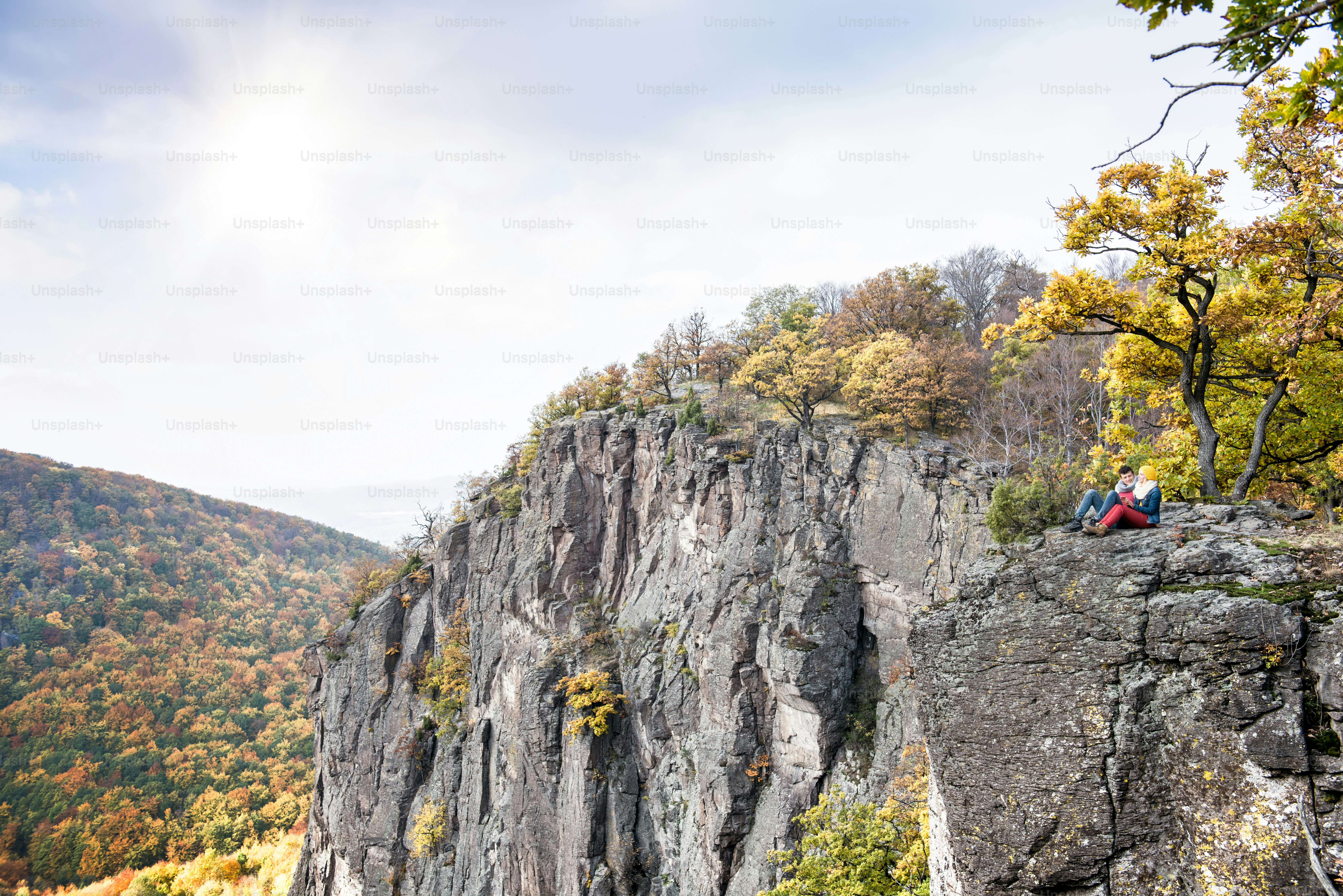 Beautiful couple in autumn nature sitting on a rock against colorful autumn forest