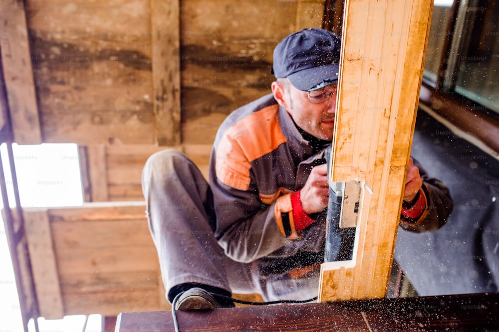 Falegname con smerigliatrice. Uomo che macina assi di legno per la costruzione di case.