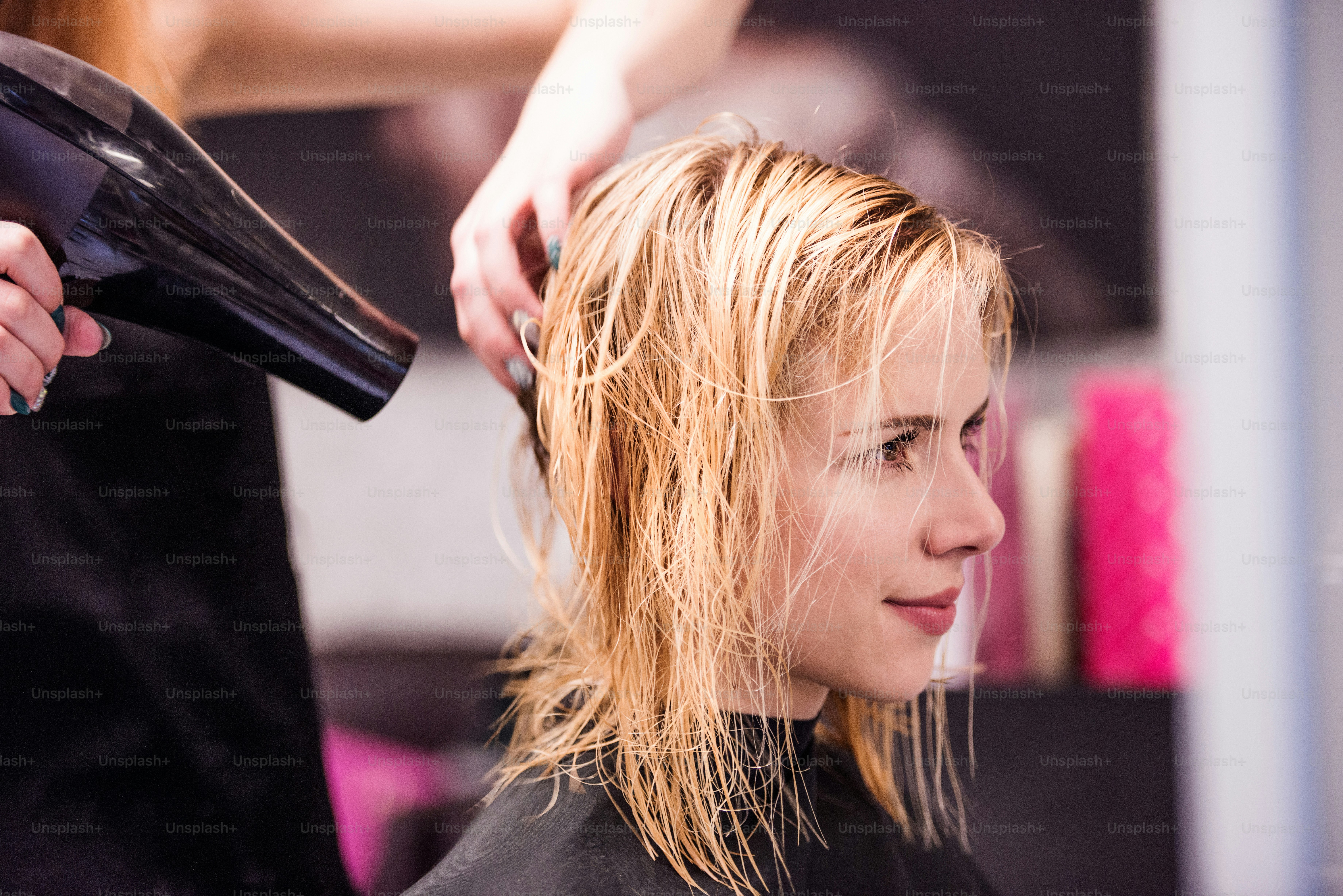 Hände des nicht erkennbaren professionellen Friseurs trocknen Haare ihres Kunden, neuer Haarschnitt, blonde Kundin.