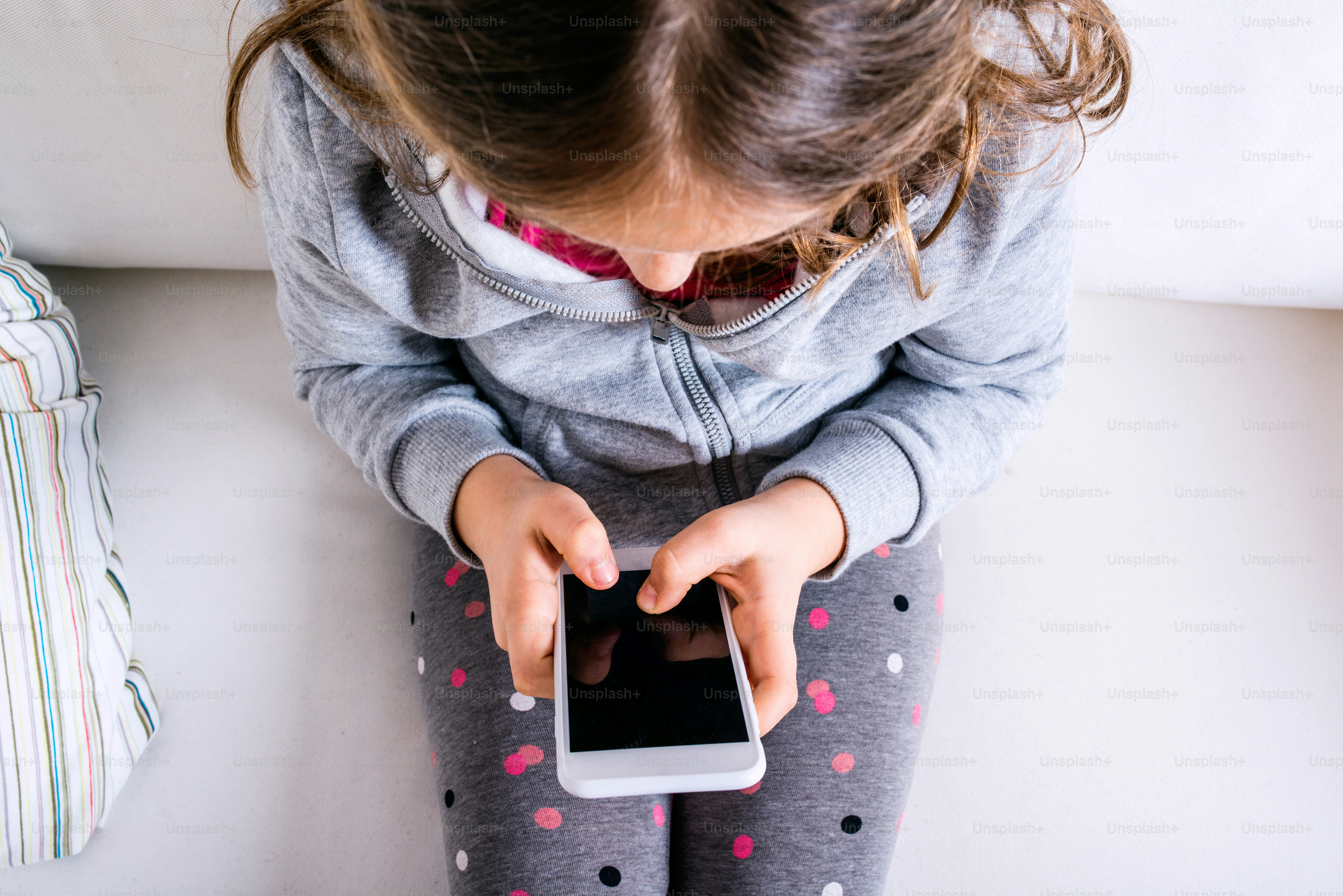 Little girl sitting on sofa with a smart phone. Happy child playing indoors.