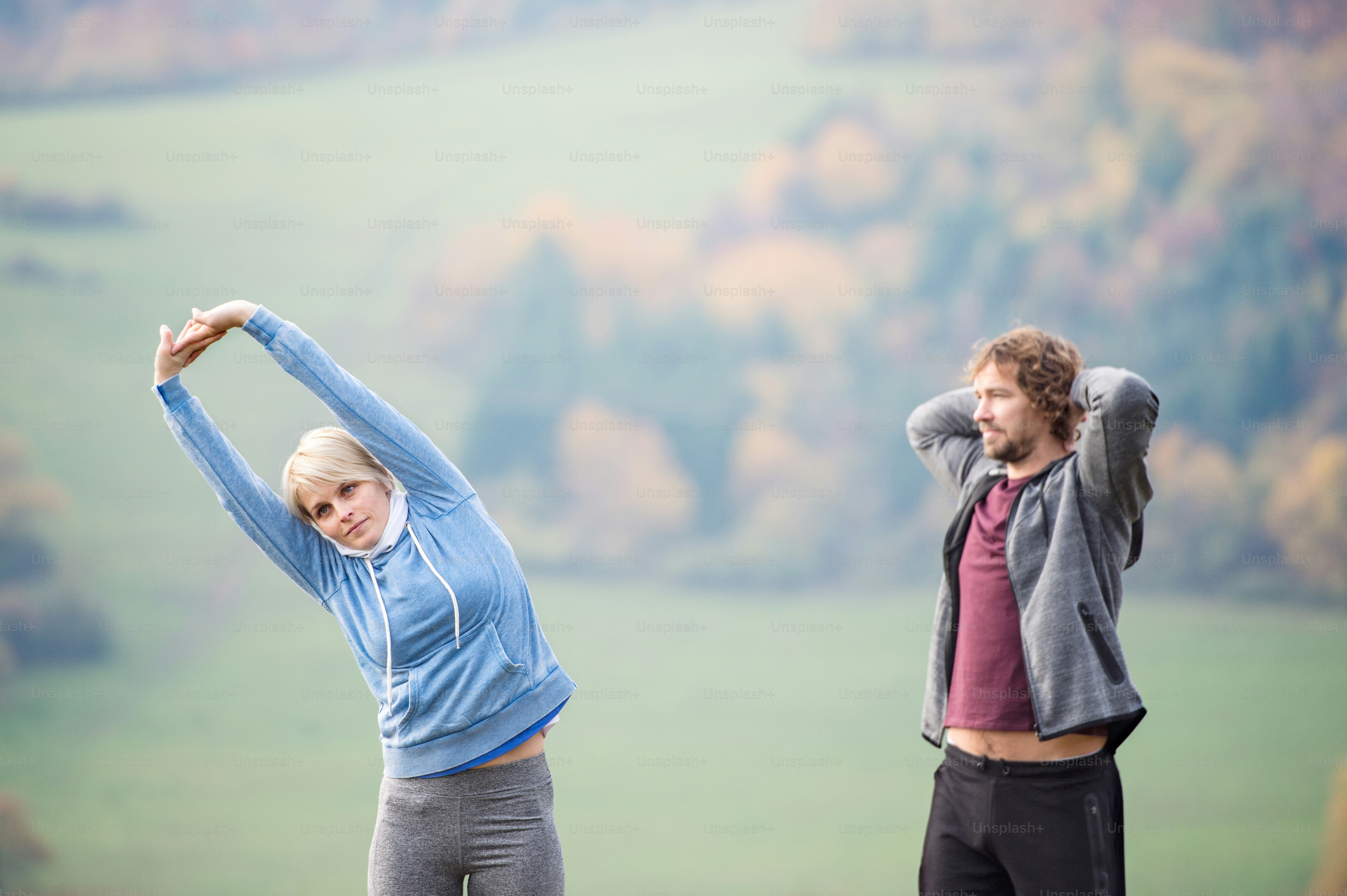 Two young beautiful runners in colorful autumn nature, stretching arms