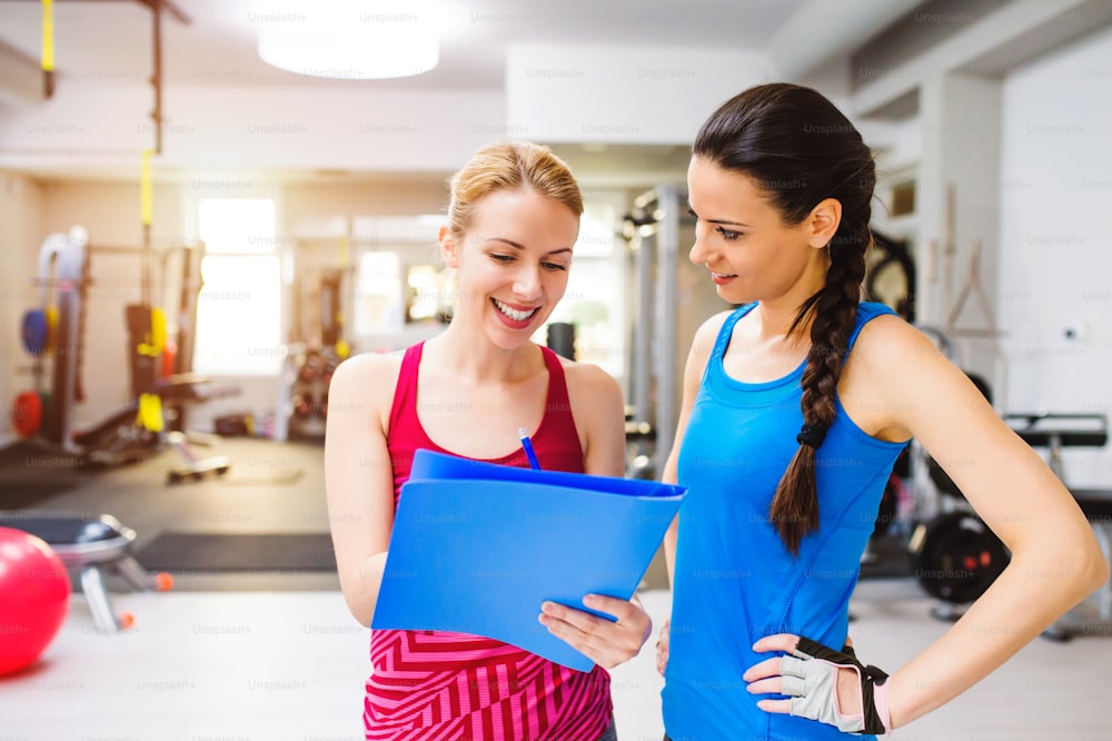 클로즈업, 체육관 컨설팅에서 매력적인 맞는 여성은 개인 트레이너와 함께 운동하고, 클립보드에 운동 계획을 세웁니다.