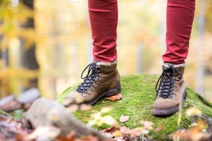 Close up of legs of unrecognizable woman in autumn nature standing on a rock covered with green moss. Hiking shoes.