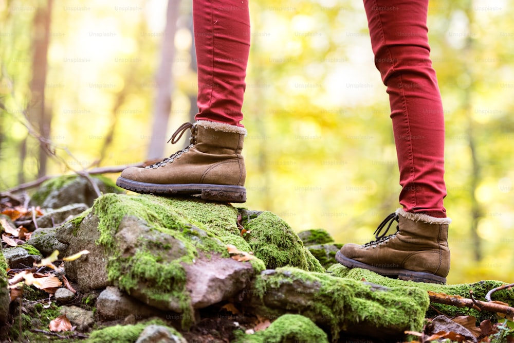 Gros plan des jambes d’une femme méconnaissable dans la nature d’automne debout sur un rocher recouvert de mousse verte. Chaussures de randonnée.