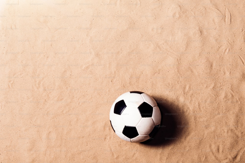 Soccer ball laid on beach. Summer vacation composition. Sand background, studio shot, flat lay. Copy space.