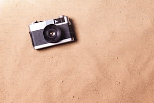 ビーチに置かれたビンテージカメラ。夏休みの構図。砂の背景、スタジオショット、フラットレイ。スペースをコピーします。