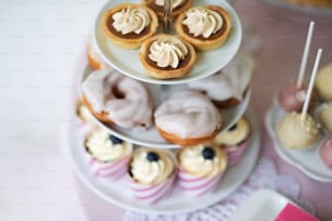 Tarts with meringues, glazed cream puffs or profiterole and cupcakes on cakestand. Cake pops on plate.