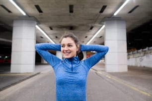 Beautiful young runner under the bridge in the town in the evening warming up and stretching arms