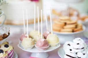 ケーキスタンド、メレンゲ、カップケーキの上に白とピンクのケーキポップが置かれたテーブル。キャンディーバー。