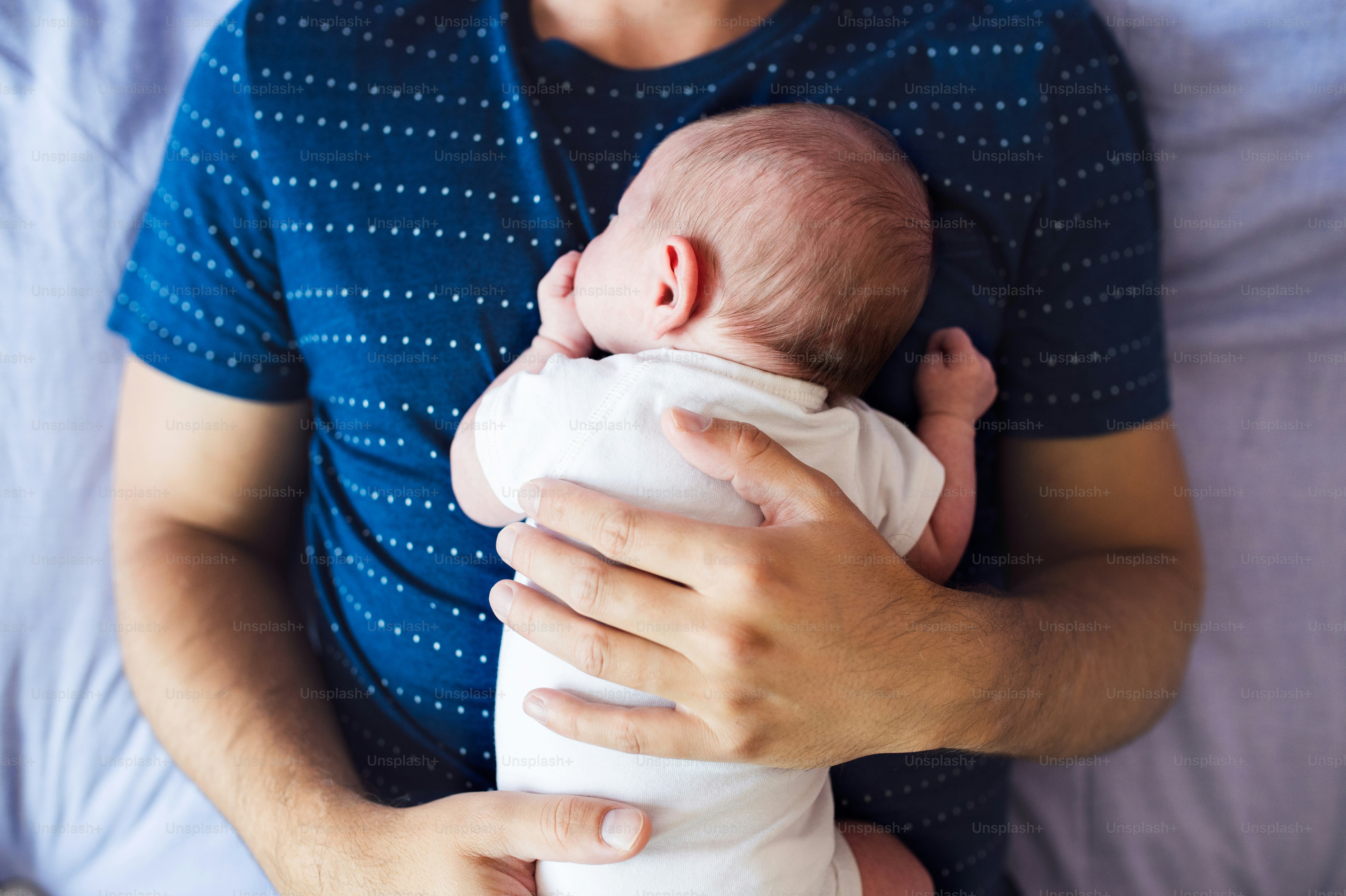Unrecognizable young father with his newborn baby son, lying on bed in bedroom