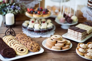 さまざまなクッキー、タルト、ケーキ、カップケーキ、ケーキポップを備えた茶色の木製のテーブル。スタジオ撮影。