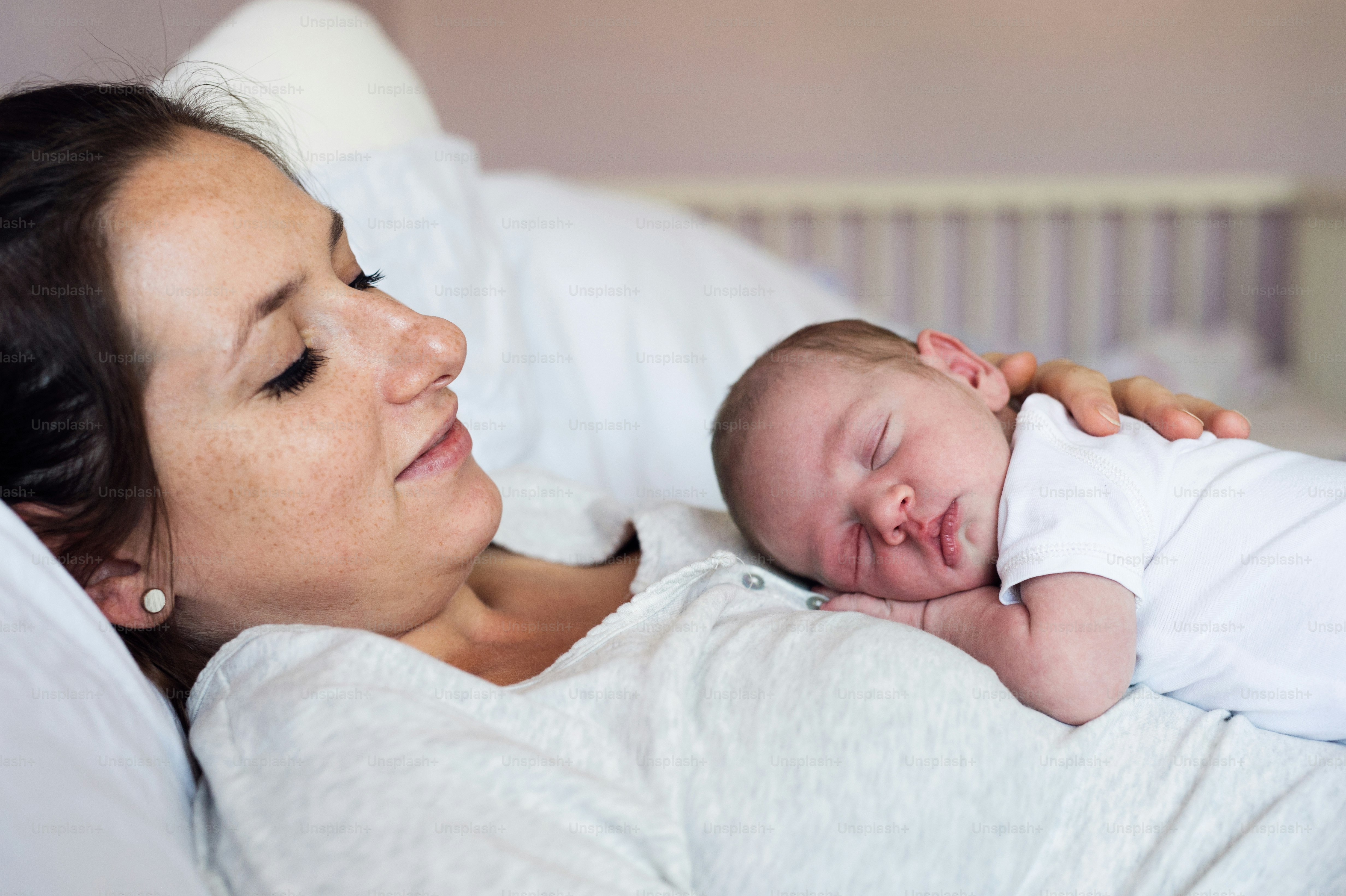 Beautiful young mother with her newborn baby son lying in bed in bedroom