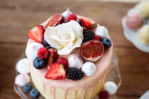 Cake with various berries, figs, meringues and white rose on top. Studio shot. Wooden background.