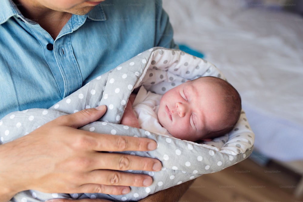 Unrecognizable young father holding his newborn baby son. Close up.