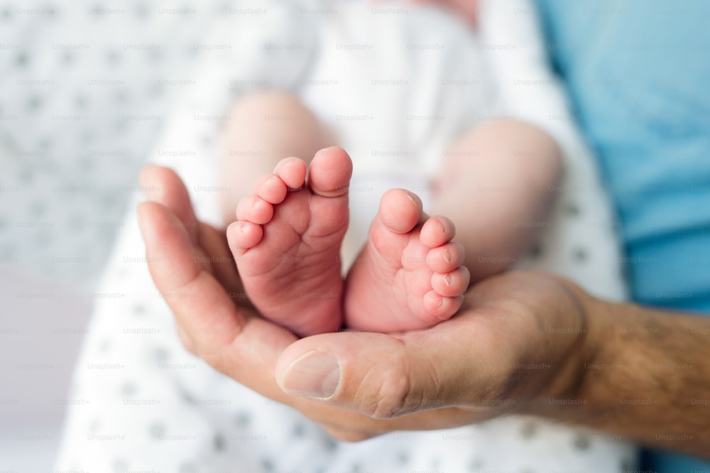 Unrecognizable father with newborn baby son, legs and hand. Close up.