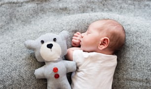 Cute little newborn baby boy lying on bed with his teddy bear, sleeping, close up
