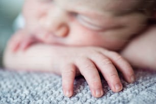 Cute little newborn baby boy lying on bed, sleeping, close up of his hand with little fingers