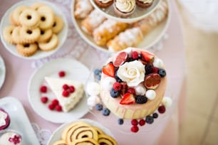 Cake with various berries and meringues on a stand. Cupcakes, cookies and tubes of pasty on other stands. Studio shot.