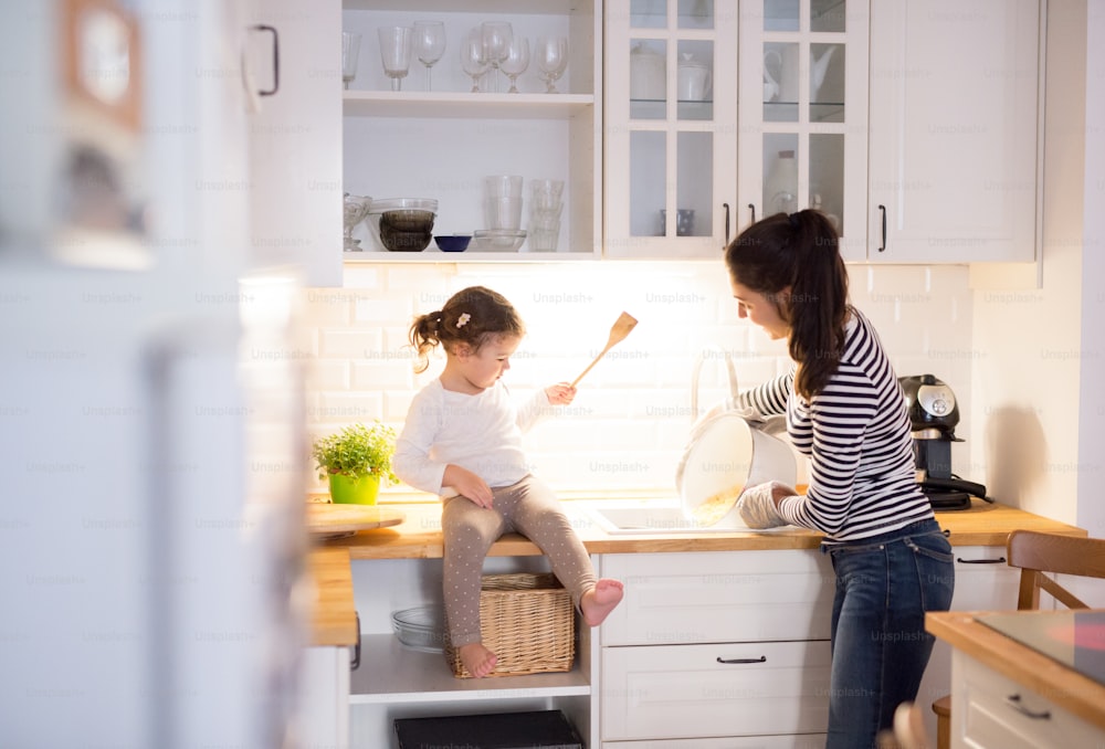 Schöne junge Mutter mit ihrer süßen kleinen Tochter in der Küche, die zusammen Pasta kocht