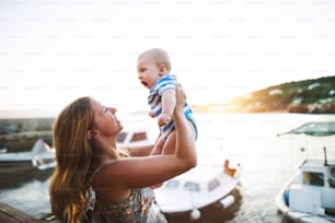 赤ん坊の息子を腕に抱いて海辺での時間を楽しんでいる美しい若い女性。