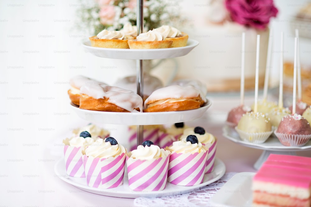 Tartas con merengues, hojaldres de crema glaseada o profiterol y cupcakes en soporte para pasteles. Cake pops en plato.