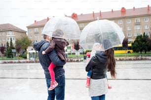 Belle jeune famille avec deux petites filles sous les parapluies, en ville un jour de pluie. Vue arrière