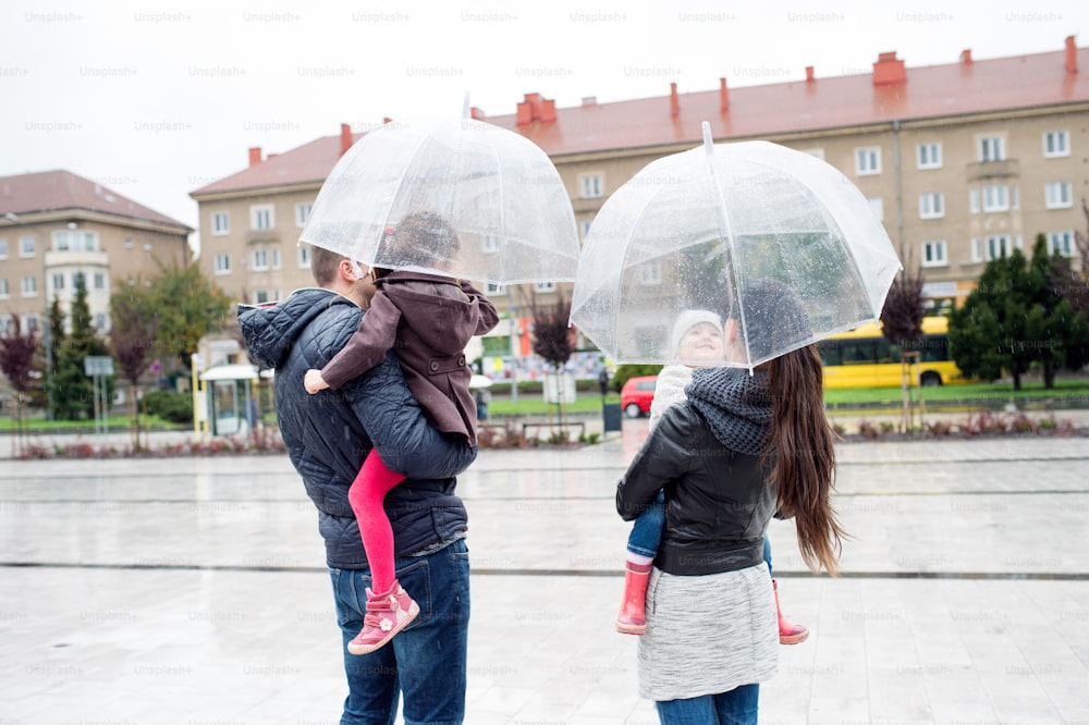 Beautiful young family with two little daughters under the umbrellas, in town on a rainy day. Rear view