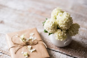 꽃병에 아름 다운 화이트 라일락 꽃다발이 테이블에 누워 갈색 종이에 싸여 선물. 흰색 나무 배경에 스튜디오를 촬영했습니다.