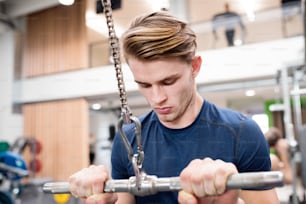 Young handsome fit man working out on pull-down machine in gym. Bodybuilder exercising with cable weight machine.