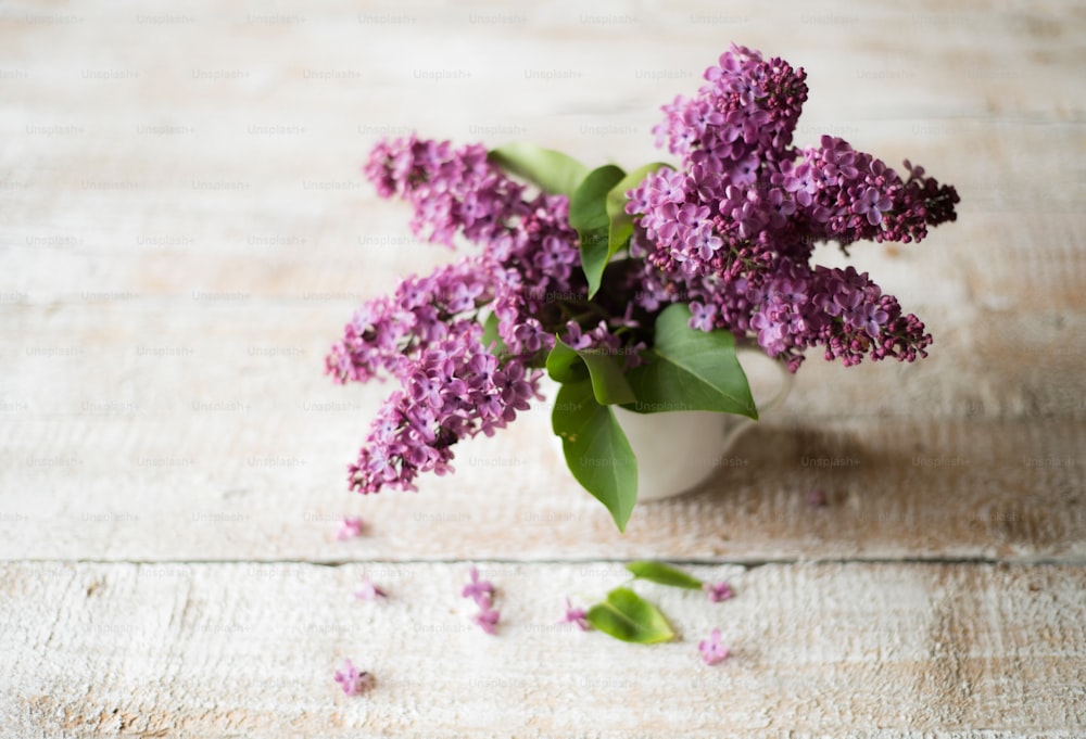 Beautiful lilac bouquet in vase laid on table. Studio shot on white wooden background.