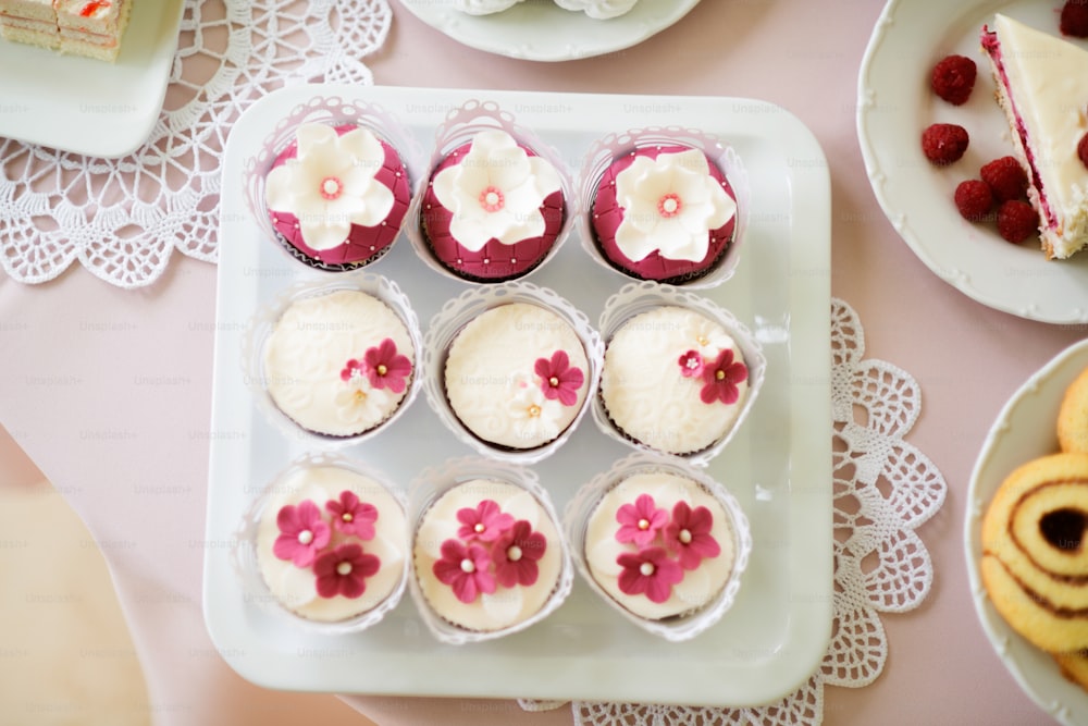 Close up, cupcakes on tray decorated with white and pink flowers laid on table with pink tablecloth and handmade lace. Candy bar.