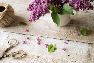 Beautiful purple lilac bouquet, scissors and  in vase laid on table. Studio shot on white wooden background.