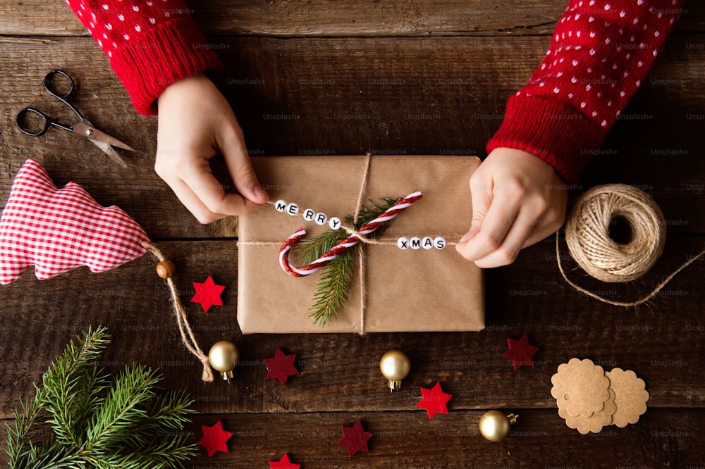 Hände einer nicht erkennbaren Frau, die Weihnachtsgeschenke einwickeln und dekorieren, liegen auf einem Holztischhintergrund. Studioaufnahme.
