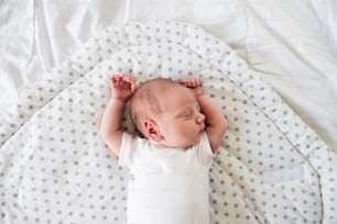 Süßer kleiner neugeborener Junge, der auf dem Bett liegt, schläft, die Hände hoch. Aufschließen.