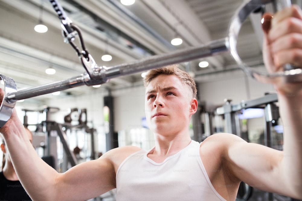 Young handsome fit man working out on pull-down machine in gym. Bodybuilder exercising with cable weight machine. Close up.