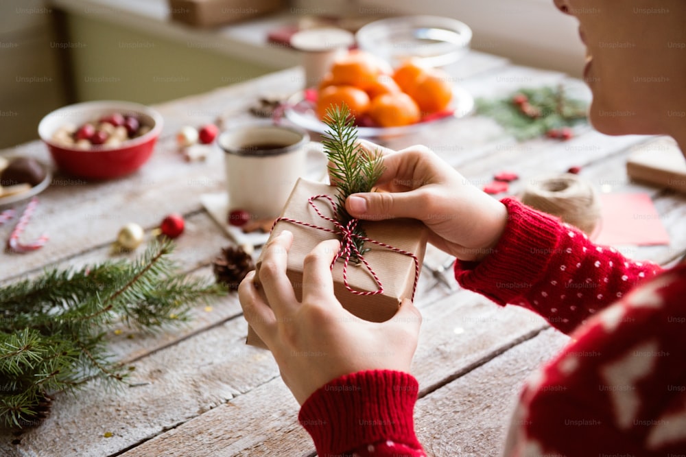 Mãos de mulher irreconhecível embrulhando e decorando o presente de Natal contra o fundo da mesa de madeira. Foto de estúdio.