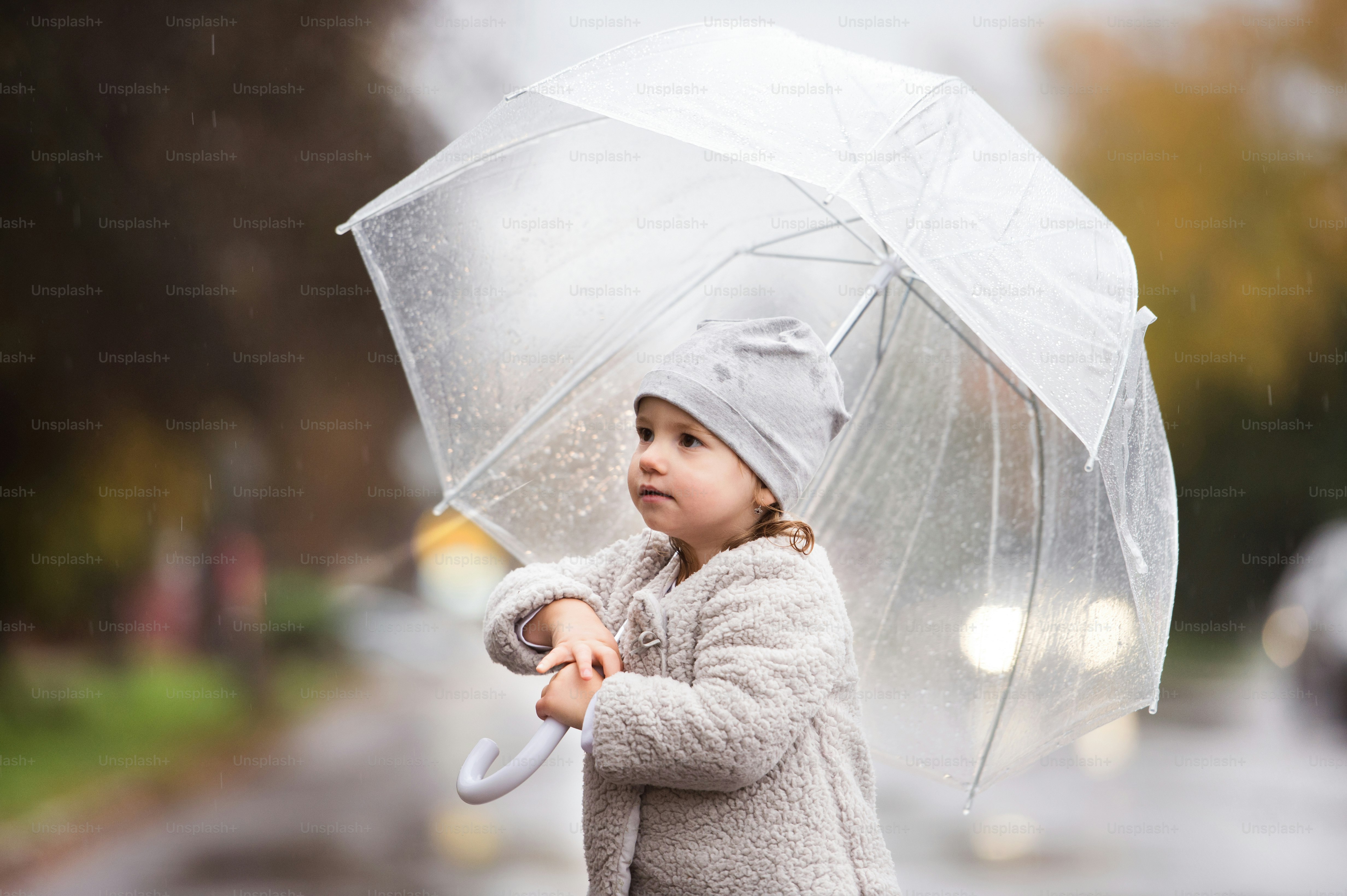Cute little girl under the transparent umbrella in town on a rainy day. Rear view.
