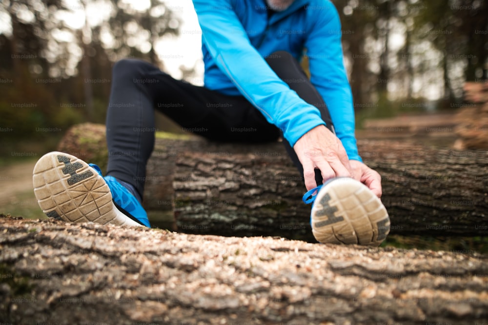 Unrecognizable runner in nature. Man sitting on wooden logs, resting, stretching, tying shoelaces.