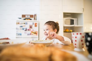 Cute little girl sitting at the table in the kitchen, eating breakfast