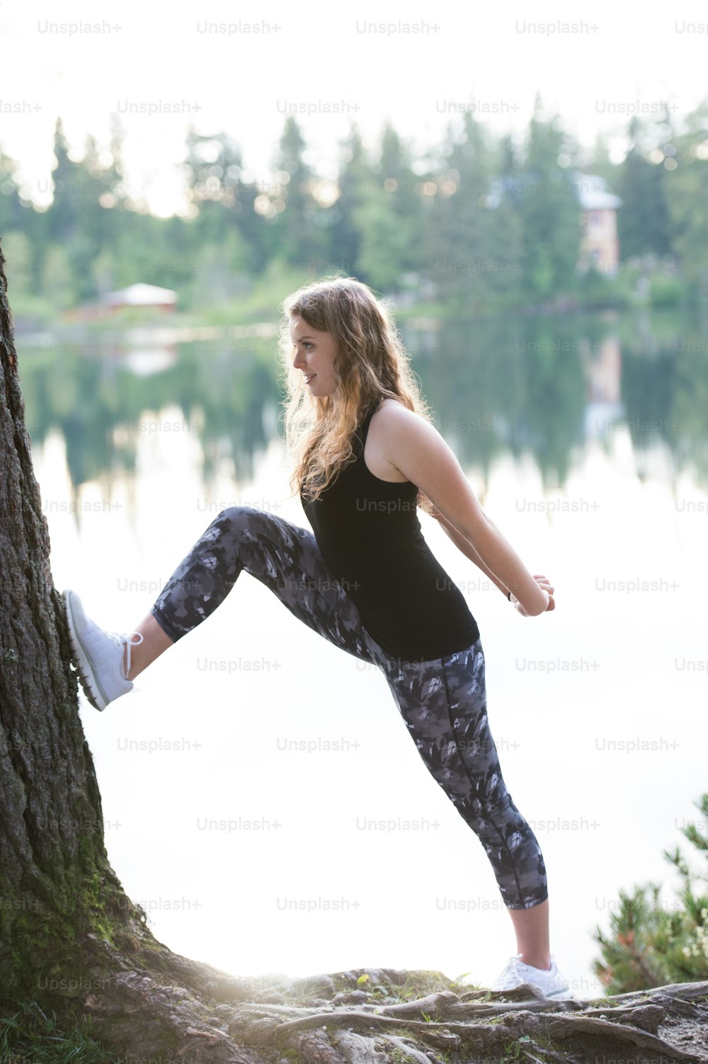 Beautiful young woman at the lake in green nature, stretching and warming up.