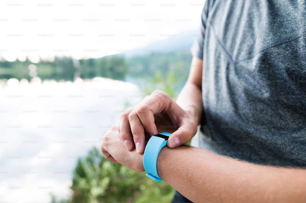 Close up of unrecognizable runner at the lake in green nature wearing smartwatch. Using a fitness app for tracking weight loss progress, running goal or summary of his run.