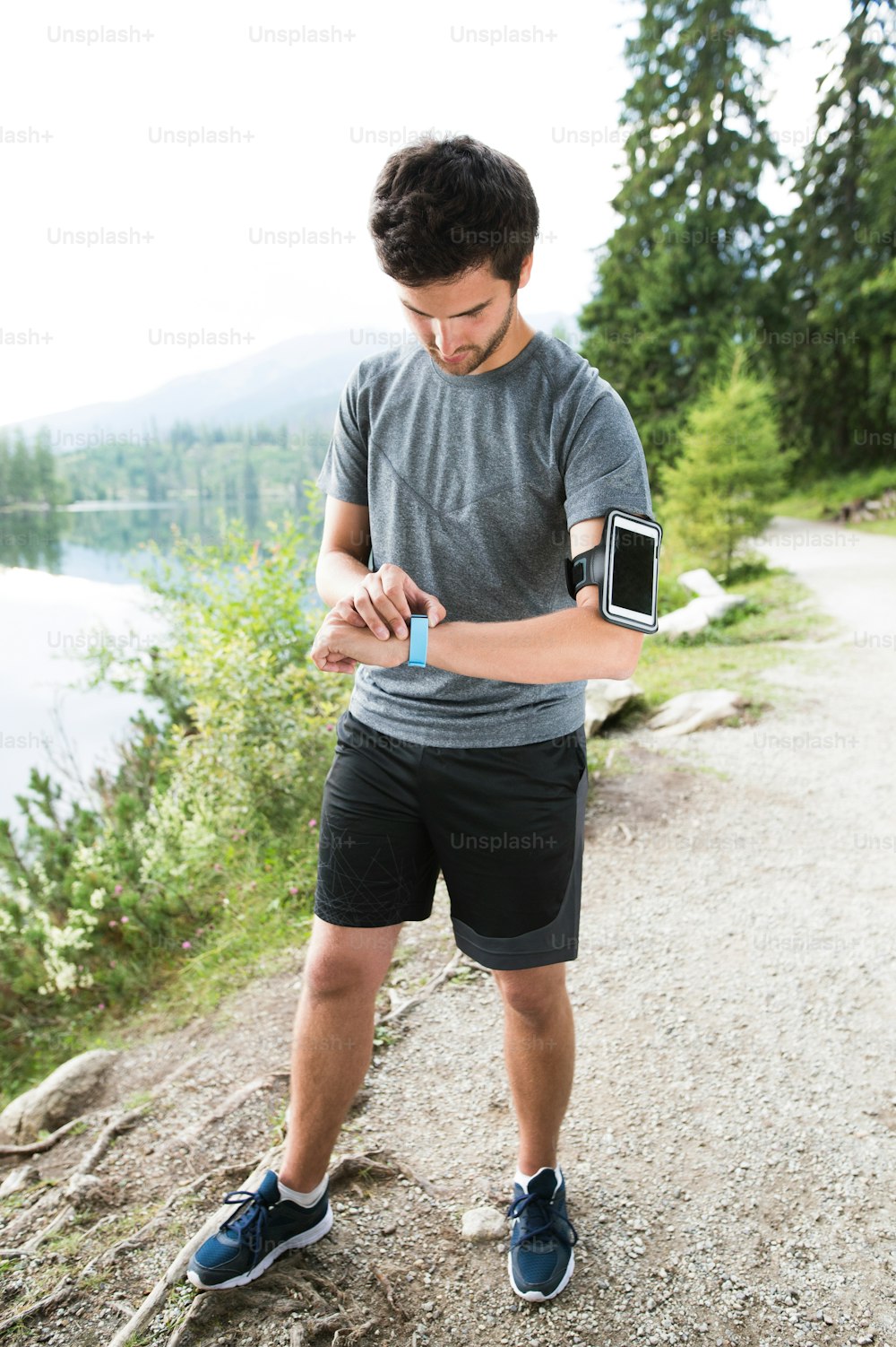 Jovem corredor no lago na natureza verde com smartphone e smartwatch. Usando um aplicativo de fitness para acompanhar o progresso da perda de peso, meta de corrida ou resumo de sua corrida.