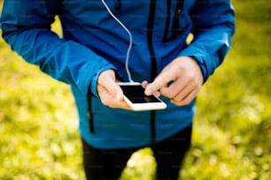 Corredor irreconhecível do lado de fora na natureza ensolarada do outono usando um aplicativo de fitness em seu smartphone. Usando o aplicativo de telefone para acompanhar o progresso da perda de peso, meta de corrida ou resumo de sua corrida.