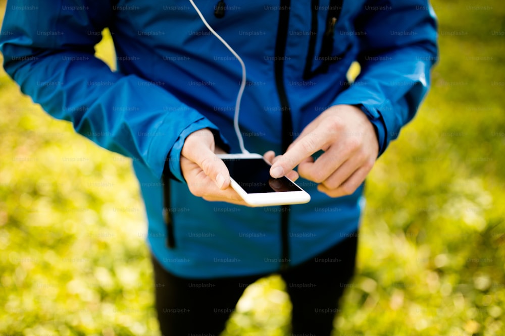 晴れた秋の自然の中、スマートフォンのフィットネスアプリを使って外を走るランナー。減量の進捗状況、ランニングの目標、またはランニングの概要を追跡するための電話アプリを使用します。