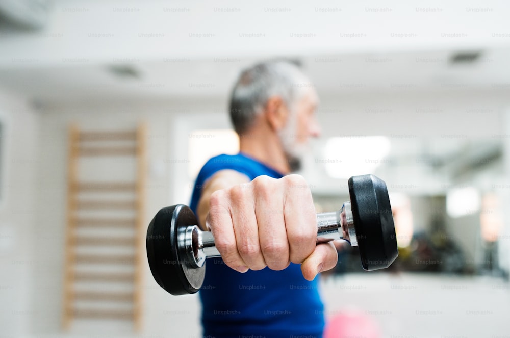 Uomo anziano in abbigliamento sportivo in palestra che si allena con i pesi. Primo piano delle mani.